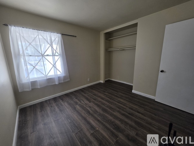 A room with a window covered by a white curtain and a wooden floor.