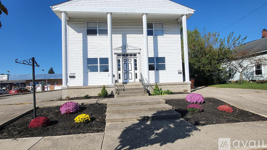 A white building with a porch and flower beds in front.