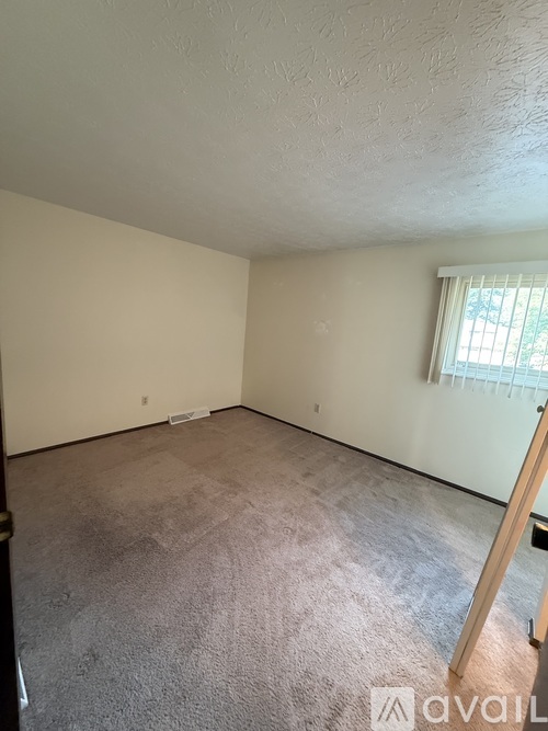 A room with a carpeted floor and a window with blinds.