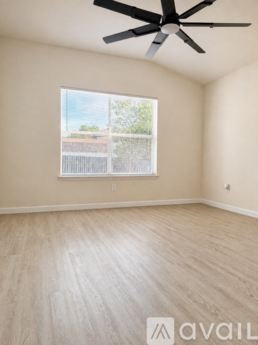 A room with a ceiling fan and light, hardwood floors, and a window with a view of a fence and trees.