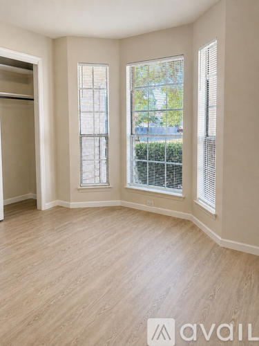 A room with wooden flooring and two windows with blinds.