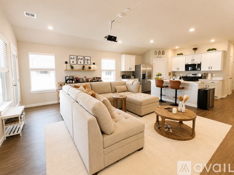 A modern living room with a large beige sofa and a kitchen area in the background.