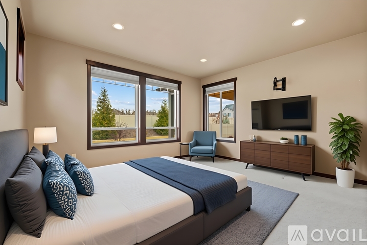 A bedroom with a large bed, a chair, a TV, and a window overlooking a tree-filled landscape.