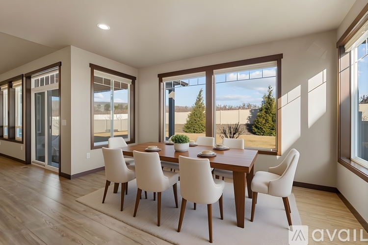 A dining room with a table and chairs and a view of the outdoors through the windows.