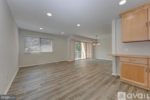 A spacious room with wooden flooring and a kitchen area with cabinets and a counter.