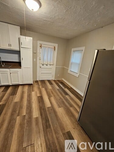 A room with wooden floors and a refrigerator on the right side.