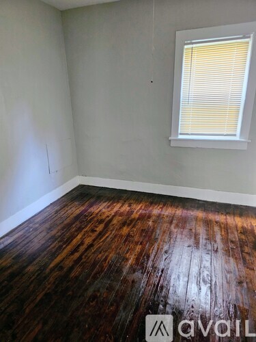 A room with wooden flooring and a window with blinds.