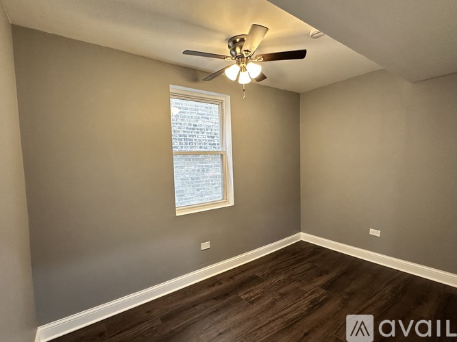 A room with a ceiling fan and a window with a view of a building.