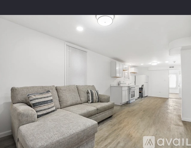 A living room with a grey couch and a kitchen in the background.