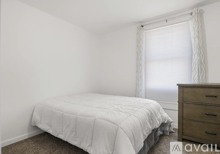 A bedroom with a white bed and a wooden dresser.