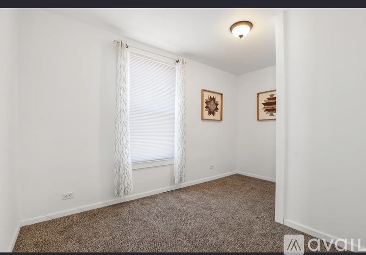 A room with a window covered by curtains and two framed pictures on the wall.