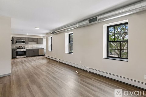 A spacious room with wooden flooring and a window with a view of trees.