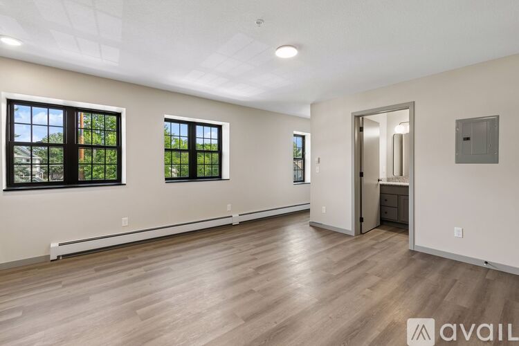 A spacious room with wooden flooring and two windows.