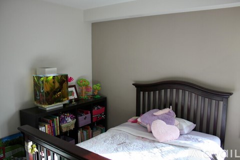 A bedroom with a bed, a nightstand with a lamp, and a bookshelf with books and toys.