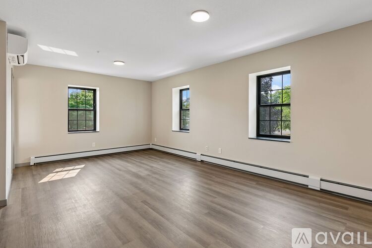 A spacious room with wooden flooring and two windows.