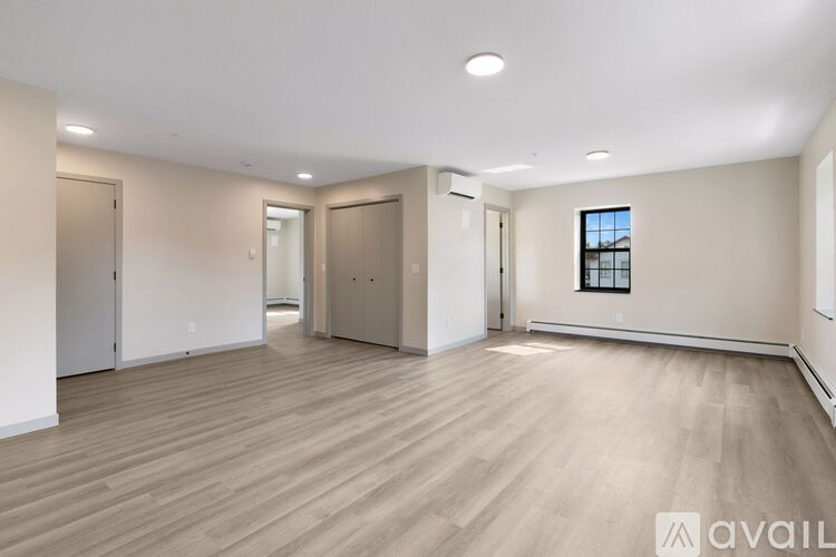 A spacious room with wooden flooring and a window on the right wall.