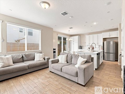 A living room with a grey couch and a kitchen in the background.
