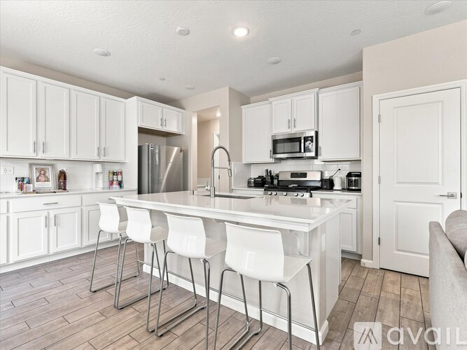 A kitchen with white cabinets and a white island with four chairs.