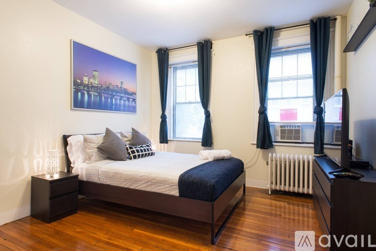 A bedroom with a large bed, a painting on the wall, and a window with curtains.