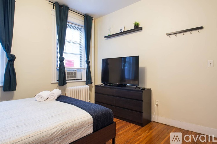 A bedroom with a bed, a television, and a window with curtains.