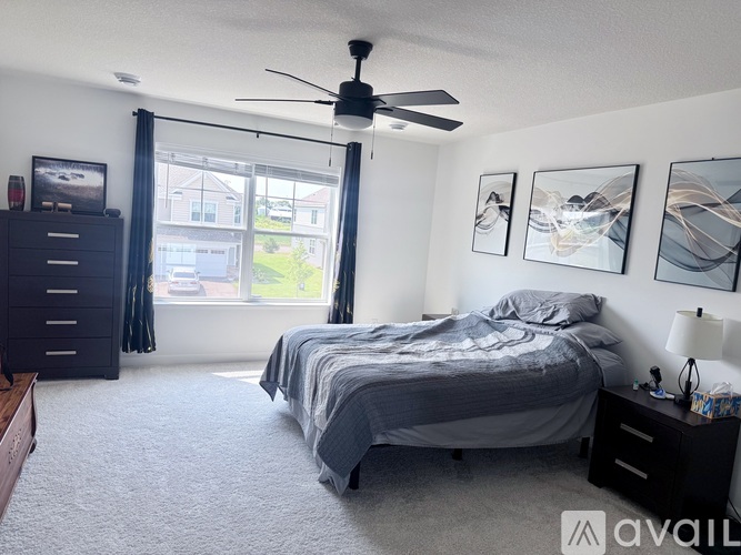 A bedroom with a large bed, a ceiling fan, and a window with curtains.