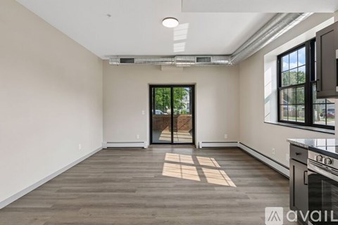 A spacious room with a wooden floor and a sliding glass door leading outside.