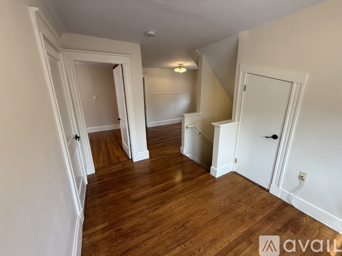 A room with wooden floors and white walls, with a doorway leading to another room.