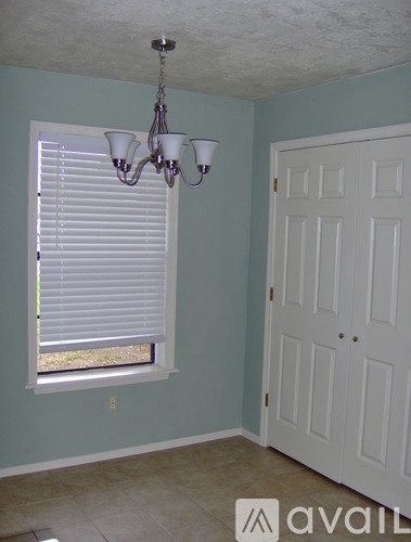 A room with a chandelier, a window with blinds, and a door.