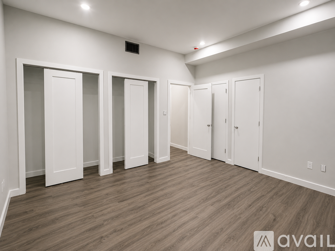 A room with white walls and wooden flooring, containing four white doors.
