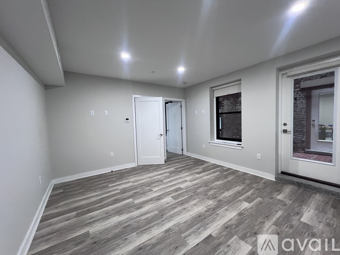 A spacious room with wooden flooring and a window with a black frame.