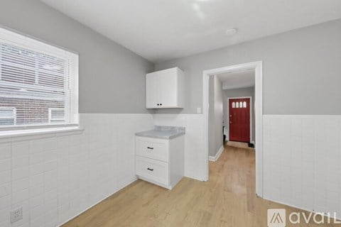 A kitchen area with white cabinets and a red door in the background.