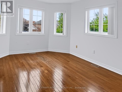 A room with wooden flooring and three windows.