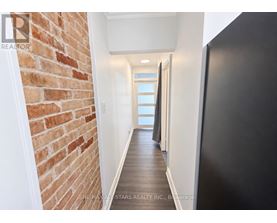 A hallway with a brick wall on the left and a black door on the right.