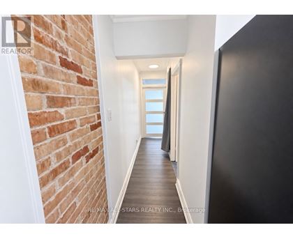 A hallway with a brick wall on the left and a black door on the right.