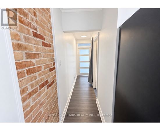 A hallway with a brick wall on the left and a black door on the right.