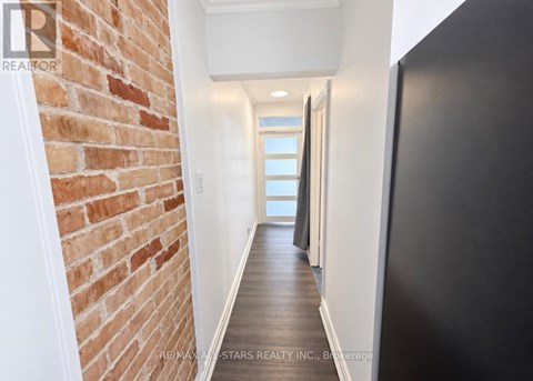 A hallway with a brick wall on the left and a black door on the right.