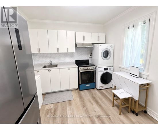 A small kitchen with a refrigerator, oven, washing machine, and dryer.