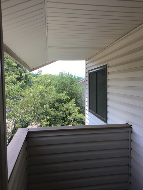 A view from the balcony of a house with a window and trees in the background.