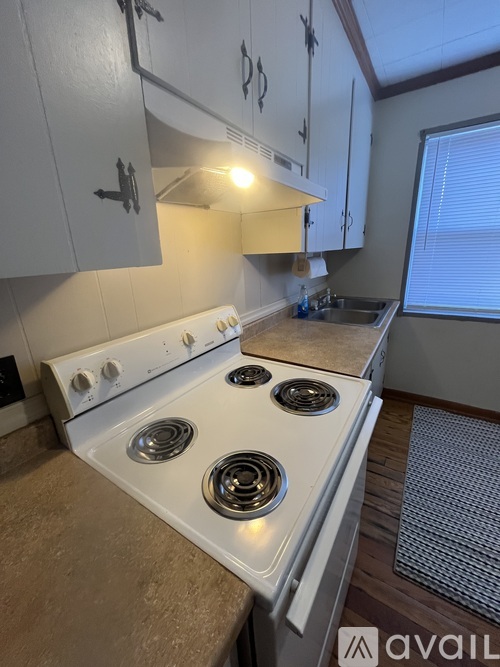 A kitchen with a white stove top oven and white cabinets.