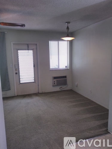 A room with a carpeted floor, a window with blinds, a door, and a ceiling fan.