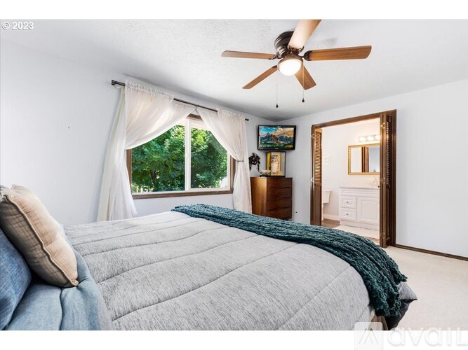 A bedroom with a bed, a ceiling fan, and a window with a view of trees.
