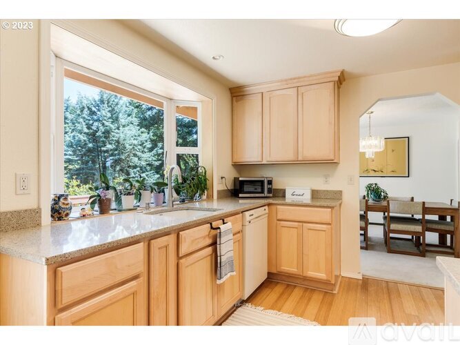 A kitchen with wooden cabinets and a window overlooking trees.