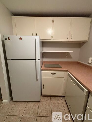 A white refrigerator stands in a kitchen with white cabinets and a brown counter.