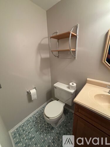 A bathroom with a toilet, sink, and a shelf above the toilet.