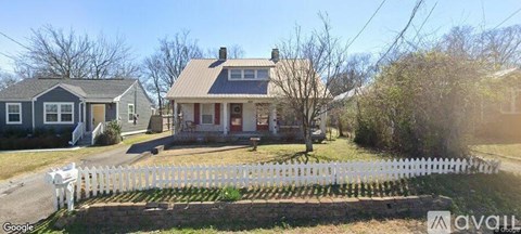 A white picket fence surrounds a house with a red door.