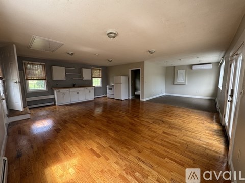 A spacious room with wooden flooring and a kitchen area in the background.