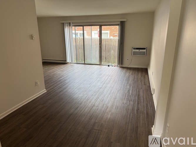 A spacious room with wooden flooring and a sliding glass door leading to a balcony.
