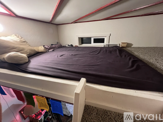 A bedroom with a bed covered in a purple blanket and a small window.