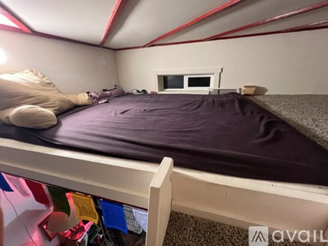 A bedroom with a bed covered in a purple blanket and a small window.