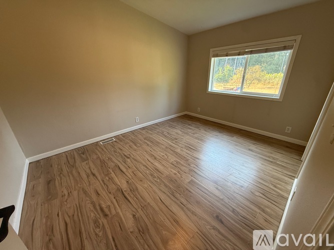 A room with wooden flooring and a window showing trees outside.